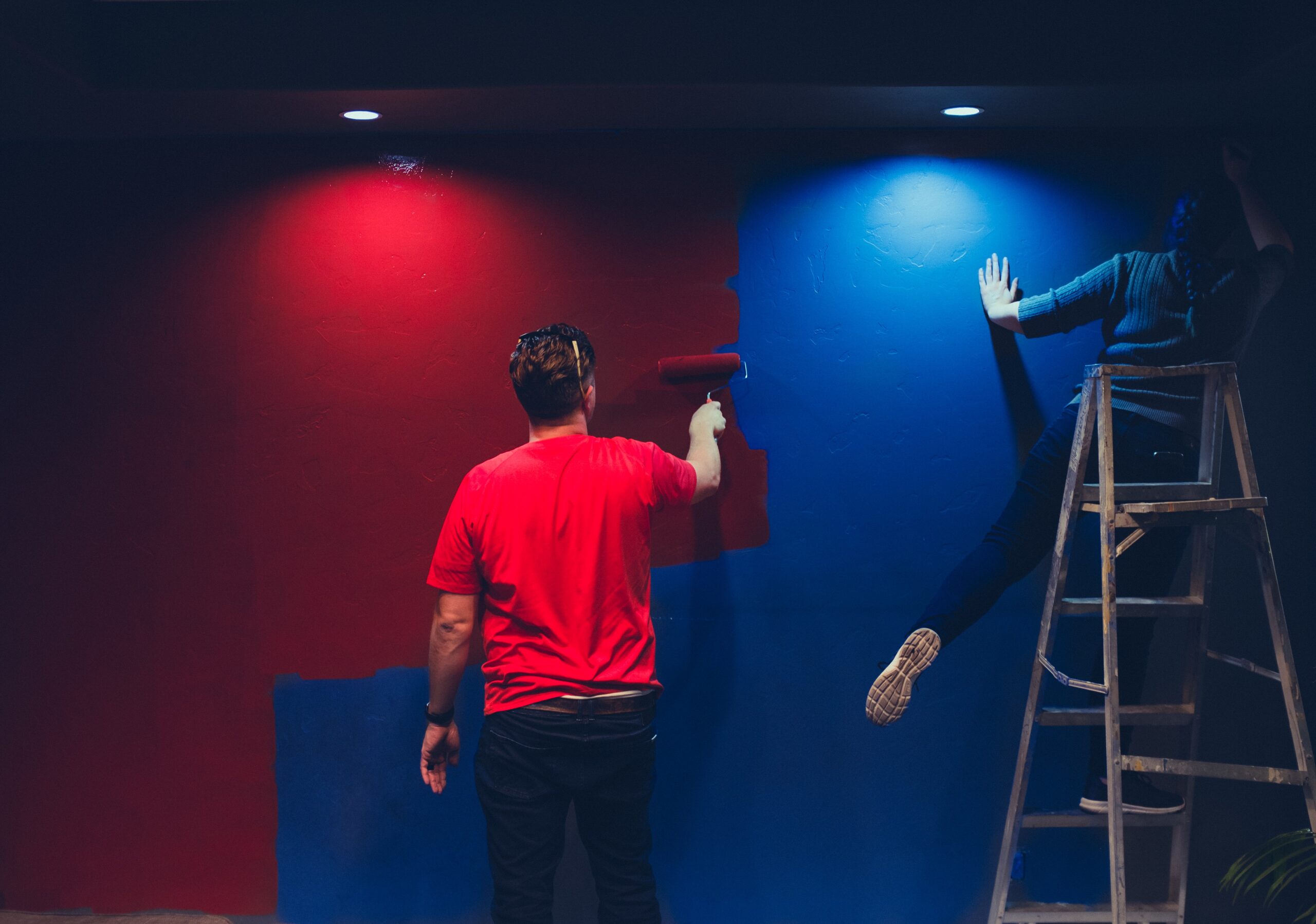 A man and a woman painting a wall red and blue